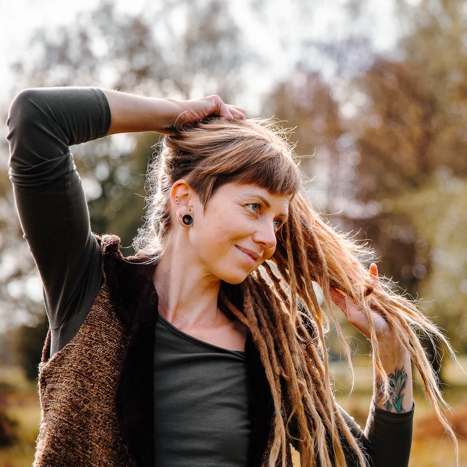 Woman with mature dreadlocks outdoors, holding her hair in natural light