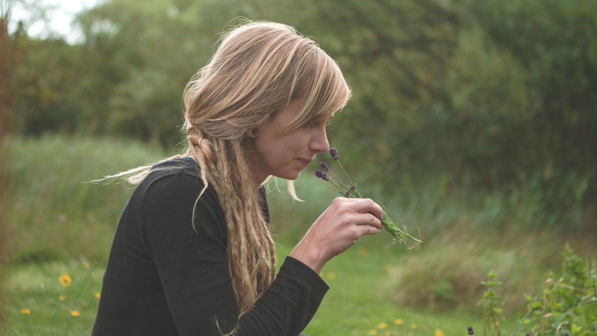 Woman with dreadlocks smelling lavender outdoors in a green natural setting